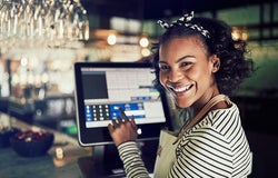 Mid shot of POS system on counter in a restaurant with female worker smiling and entering numbers