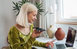 gen z female working on laptop and talking on mobile phone in her room