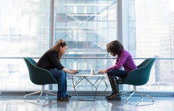 two women at a workplace sitting across a desk from each other
